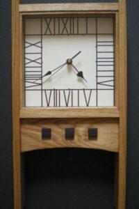 This variation of a Mackintosh mantle clock has a Hill House face and three rosewood squares on the bottom panel.